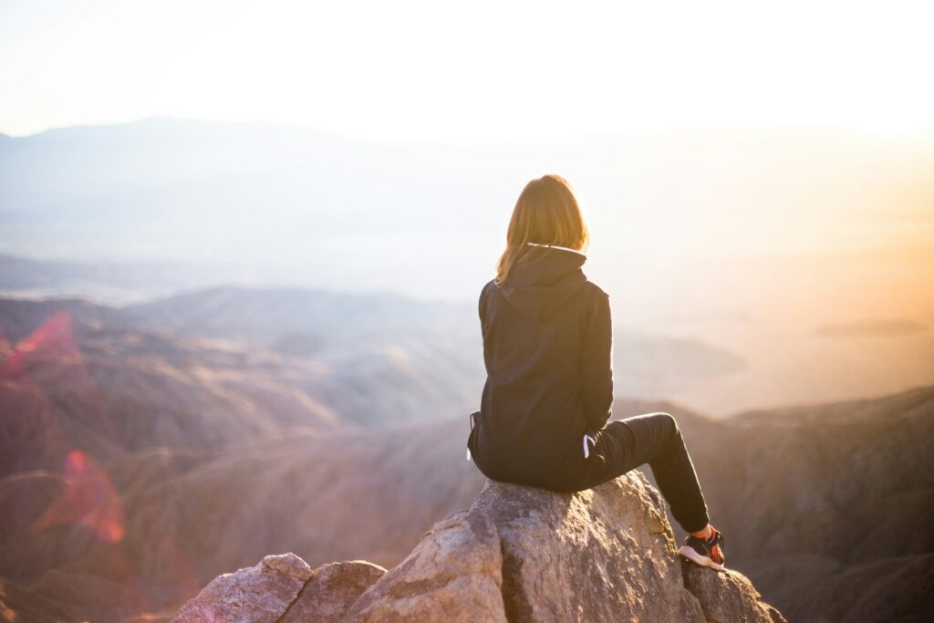 Eine Frau sitzt auf einem Felsen und blickt bei Sonnenaufgang über die Landschaft